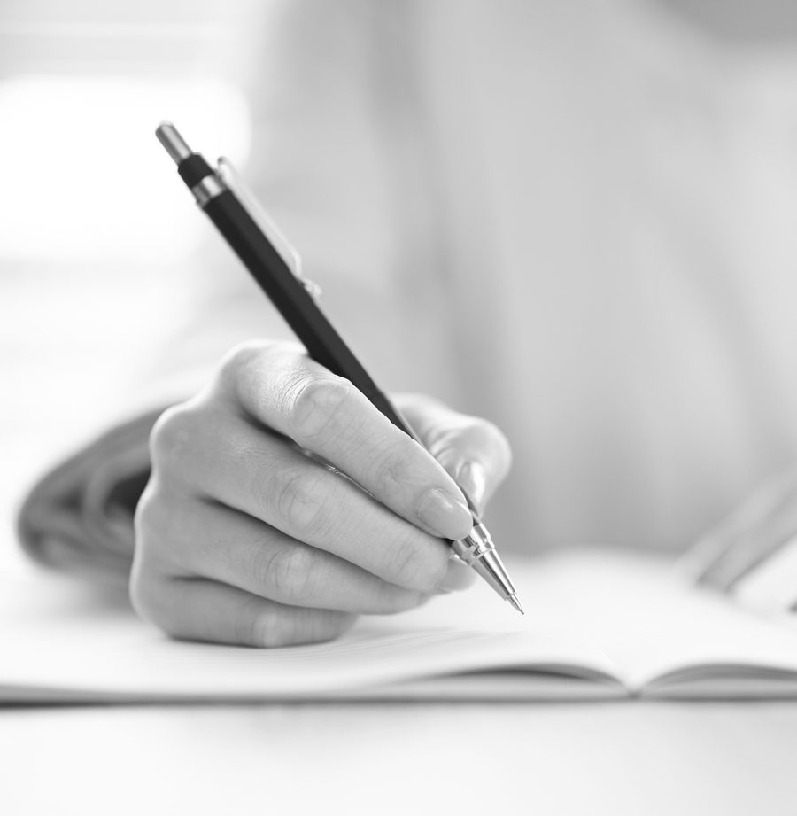ノートにペンで書き込む手元のモノクロ写真